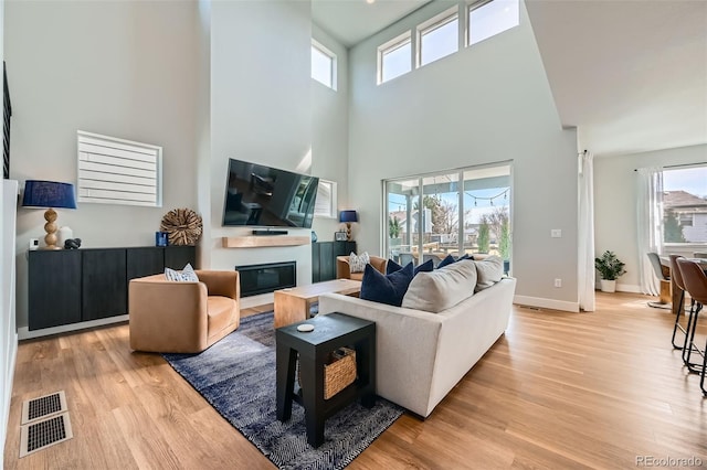 2840 E 102nd Pl, Thornton, CO 80229 - living area featuring plenty of natural light, light wood finished floors, a high ceiling, a glass covered fireplace, and baseboards