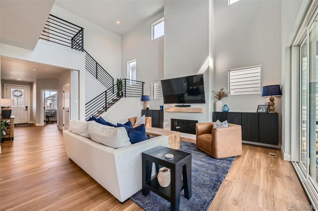 2840 E 102nd Pl, Thornton, CO 80229 - living room featuring a high ceiling, light wood finished floors, a glass covered fireplace, stairway, and recessed lighting