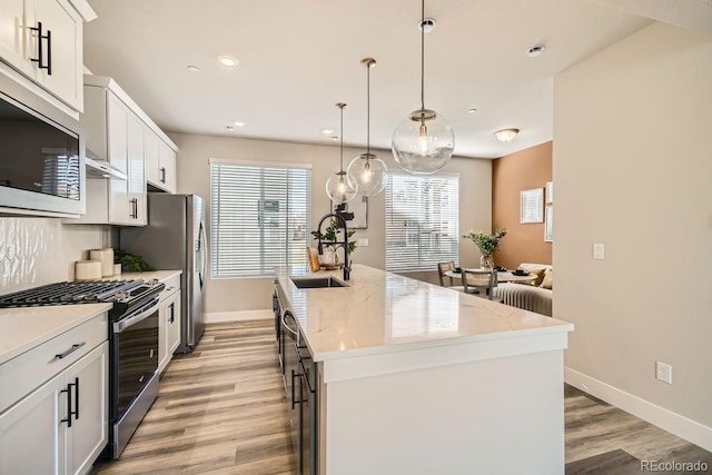 kitchen featuring hanging light fixtures, sink, white cabinets, stainless steel appliances, and a center island with sink