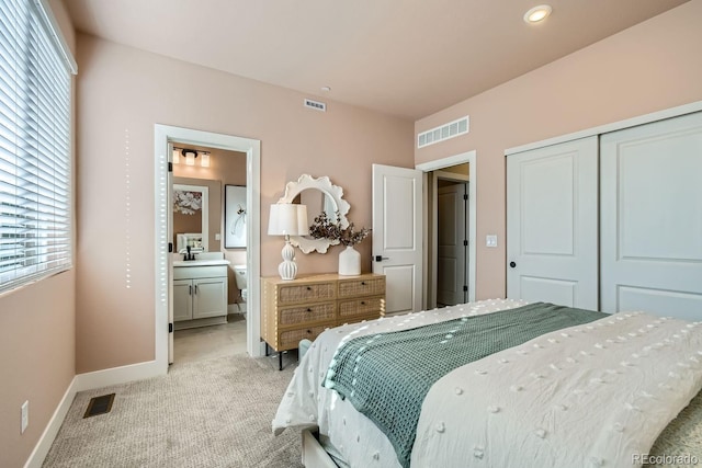 carpeted bedroom with a closet, ensuite bathroom, and sink