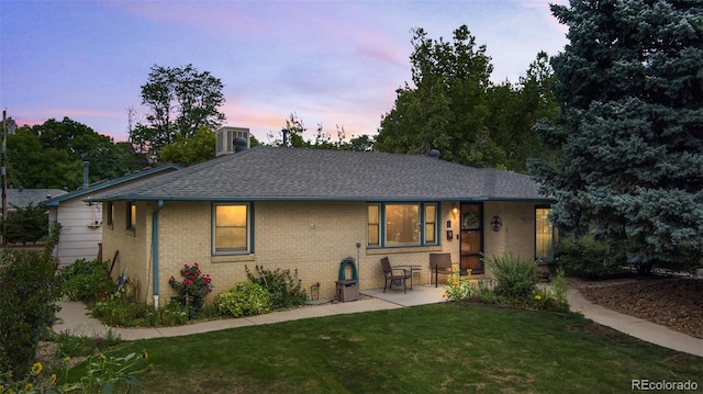 back of property with brick siding, roof with shingles, a lawn, a patio area, and cooling unit