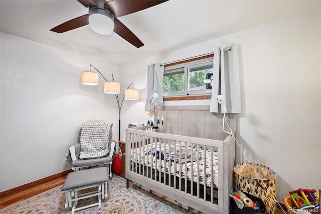 bedroom featuring a crib, baseboards, a ceiling fan, and wood finished floors