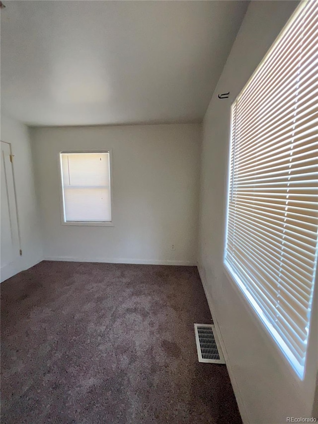 spare room featuring a wealth of natural light and dark colored carpet