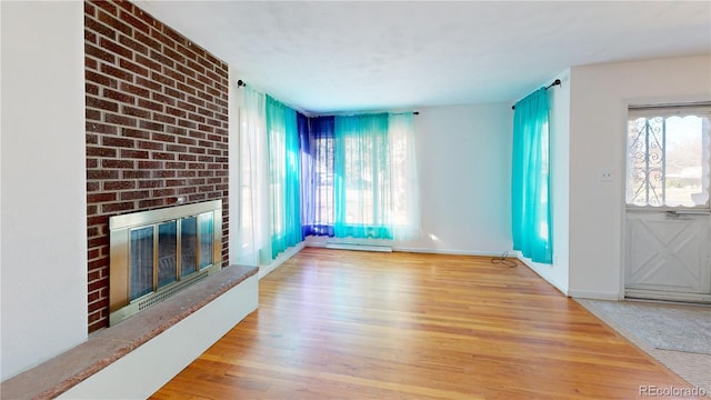 unfurnished living room with baseboards, a fireplace, a baseboard heating unit, and wood finished floors