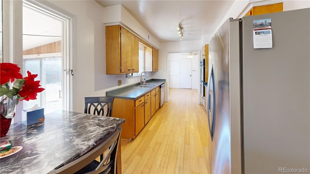 kitchen featuring light wood finished floors, stainless steel appliances, brown cabinetry, a sink, and ceiling fan