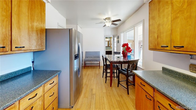 kitchen with brown cabinetry, dark countertops, stainless steel fridge, and light wood-style flooring