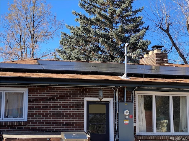 exterior space with roof mounted solar panels, a chimney, and brick siding