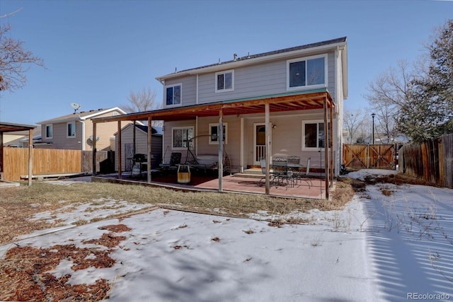 snow covered back of property with a patio area and a storage unit