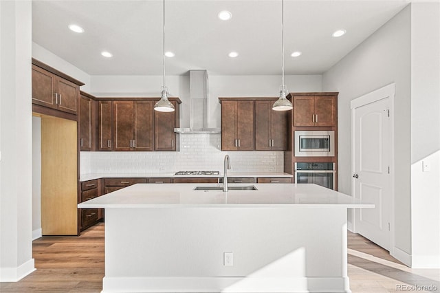 kitchen featuring hanging light fixtures, appliances with stainless steel finishes, a center island with sink, and wall chimney exhaust hood