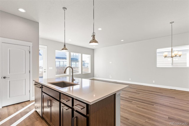 kitchen with sink, hanging light fixtures, dark brown cabinets, a center island with sink, and stainless steel dishwasher