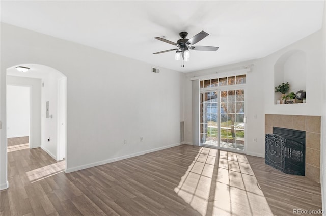 unfurnished living room featuring a tiled fireplace, hardwood / wood-style floors, and ceiling fan