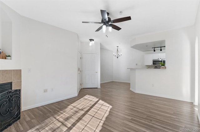 unfurnished living room featuring ceiling fan with notable chandelier, a tile fireplace, and hardwood / wood-style flooring