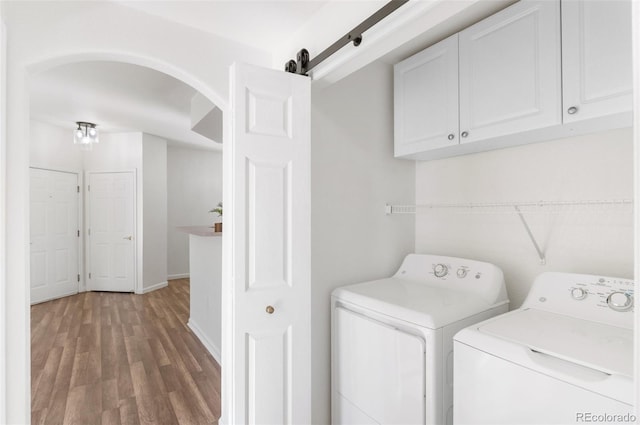 laundry room featuring washing machine and dryer, wood-type flooring, cabinets, and a barn door