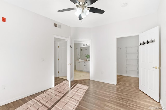 unfurnished bedroom with a closet, connected bathroom, light wood-type flooring, a walk in closet, and ceiling fan