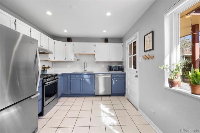 kitchen featuring appliances with stainless steel finishes, white cabinets, a sink, blue cabinets, and under cabinet range hood