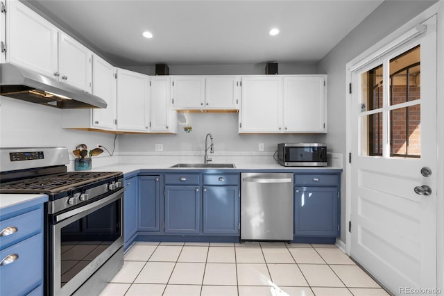 kitchen with appliances with stainless steel finishes, blue cabinetry, light countertops, under cabinet range hood, and a sink