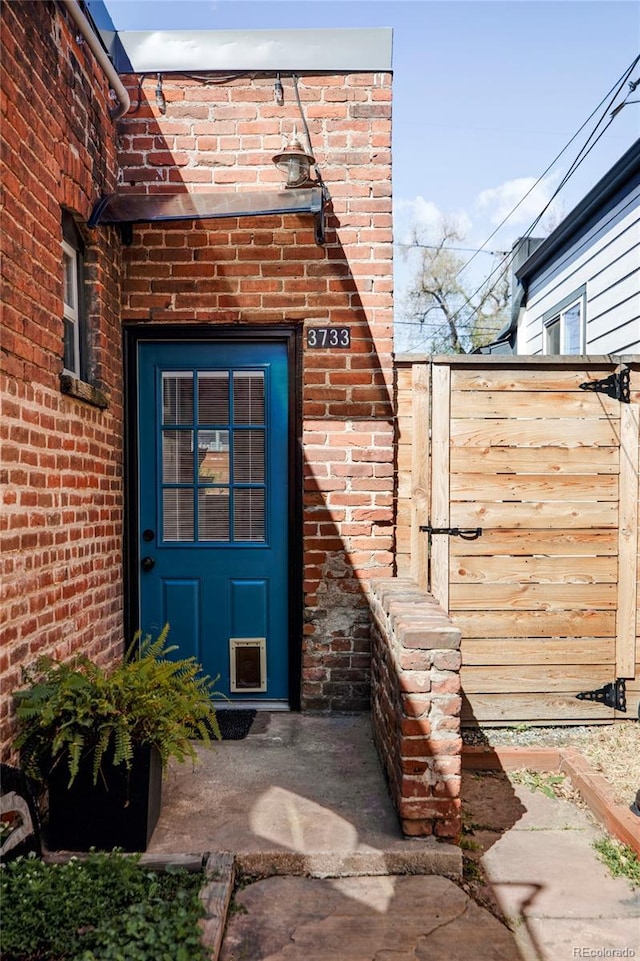 doorway to property with brick siding and fence