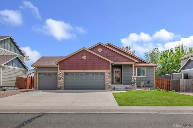 view of front facade featuring fence, an attached garage, stone siding, a front yard, and driveway