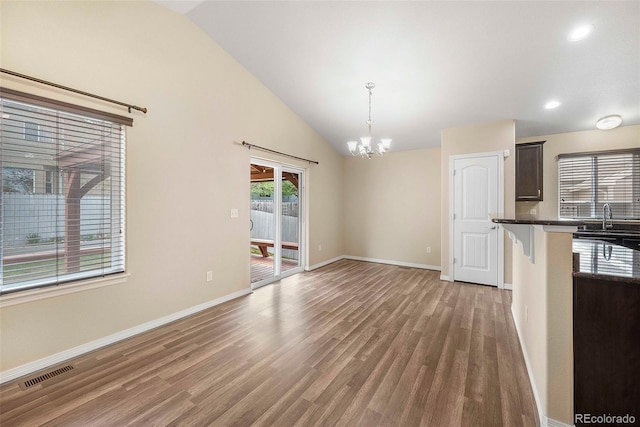 interior space featuring visible vents, wood finished floors, baseboards, a chandelier, and vaulted ceiling