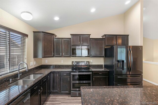 kitchen with lofted ceiling, dark stone countertops, a sink, light wood finished floors, and stainless steel appliances