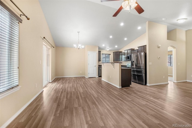 kitchen featuring appliances with stainless steel finishes, arched walkways, ceiling fan with notable chandelier, open floor plan, and a kitchen bar