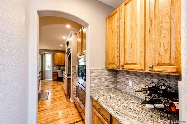 22685 E Calhoun Pl, Aurora, CO 80016 - kitchen featuring arched walkways, light wood-style floors, tasteful backsplash, light stone counters, and recessed lighting