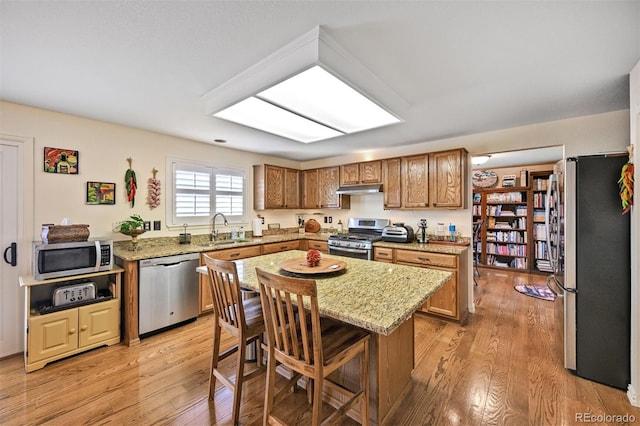 kitchen with stainless steel appliances, a sink, under cabinet range hood, light wood-style floors, and light stone counters