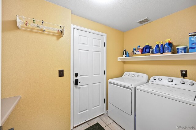 laundry room with washing machine and dryer, light tile patterned floors, and a textured wall