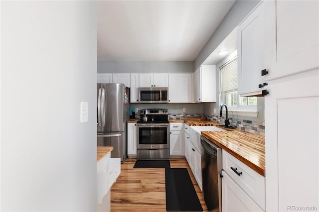 kitchen featuring white cabinets, butcher block countertops, appliances with stainless steel finishes, light wood-type flooring, and a sink