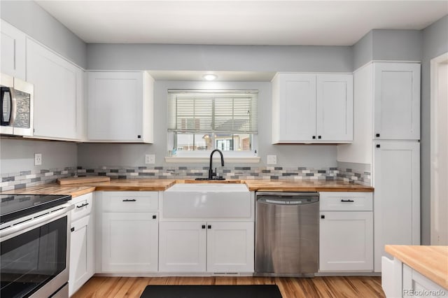 kitchen with stainless steel appliances, butcher block counters, a sink, and white cabinetry