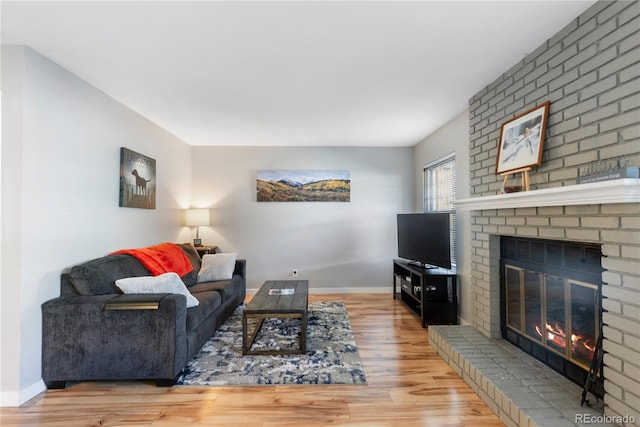 living area featuring a brick fireplace, baseboards, and wood finished floors