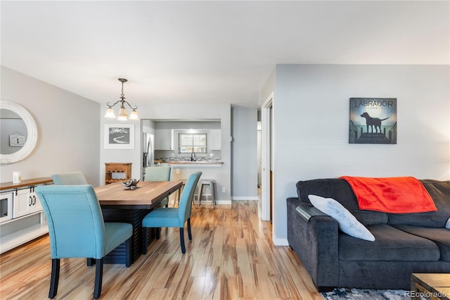 dining space featuring light wood-type flooring, a notable chandelier, and baseboards