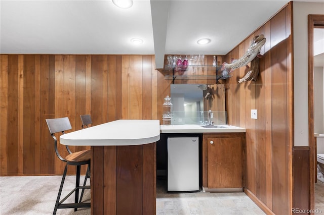 bar with wooden walls, light colored carpet, wet bar, fridge, and a sink