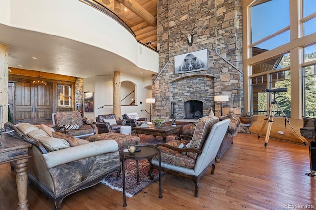 living room featuring beam ceiling, hardwood / wood-style flooring, an inviting chandelier, high vaulted ceiling, and a stone fireplace