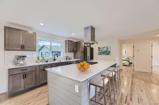 kitchen featuring island range hood, tasteful backsplash, light hardwood / wood-style flooring, and a center island