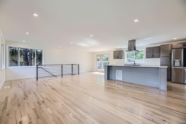 kitchen featuring wall chimney range hood, light hardwood / wood-style flooring, backsplash, stainless steel refrigerator with ice dispenser, and dark brown cabinets