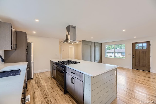 kitchen with island exhaust hood, appliances with stainless steel finishes, light hardwood / wood-style flooring, and a kitchen island