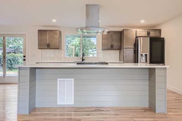 kitchen with a wealth of natural light, stainless steel fridge, island range hood, and light hardwood / wood-style flooring