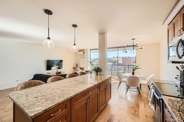 kitchen featuring light hardwood / wood-style flooring, stainless steel appliances, light stone counters, a kitchen island, and decorative light fixtures