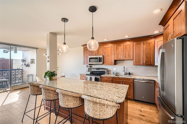 kitchen with a breakfast bar, pendant lighting, backsplash, stainless steel appliances, and light wood-type flooring