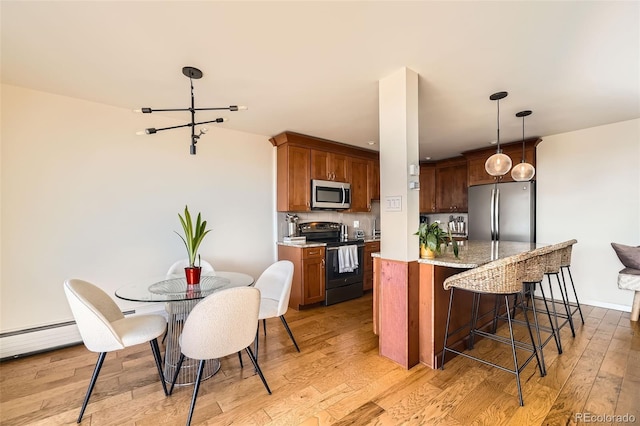 kitchen featuring hanging light fixtures, stainless steel appliances, a kitchen breakfast bar, light stone countertops, and light wood-type flooring