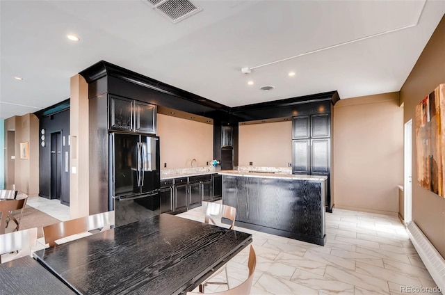 kitchen with a kitchen island, light stone countertops, black fridge, and sink