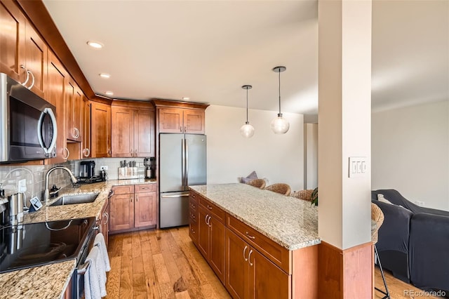 kitchen with hanging light fixtures, stainless steel appliances, a kitchen breakfast bar, light stone countertops, and light wood-type flooring