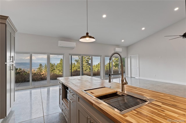 kitchen with sink, butcher block counters, an AC wall unit, vaulted ceiling, and pendant lighting