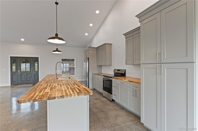 kitchen featuring butcher block countertops, appliances with stainless steel finishes, decorative light fixtures, and an island with sink