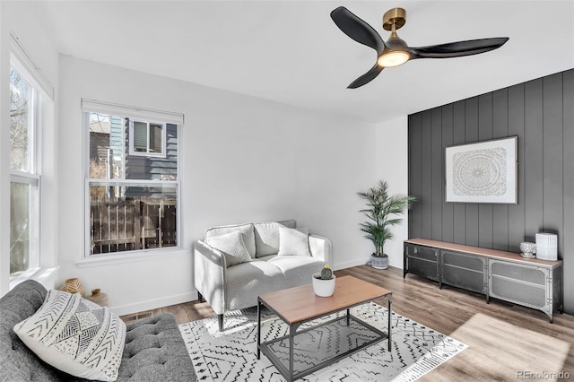 living room with hardwood / wood-style floors, ceiling fan, and wood walls