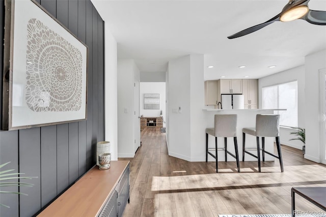 kitchen featuring gray cabinets, a kitchen breakfast bar, white fridge, ceiling fan, and light hardwood / wood-style flooring