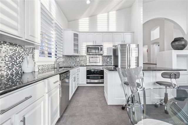 kitchen featuring appliances with stainless steel finishes, backsplash, sink, white cabinets, and lofted ceiling