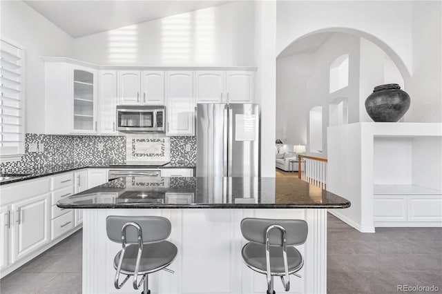 kitchen featuring white cabinets, appliances with stainless steel finishes, dark stone counters, and a breakfast bar area