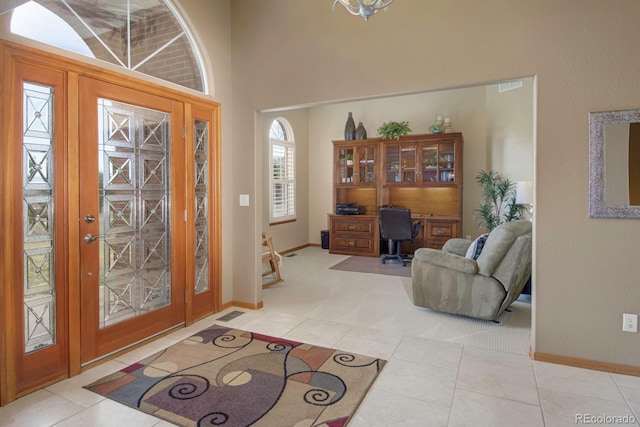 foyer entrance with visible vents, baseboards, tile patterned flooring, and a towering ceiling